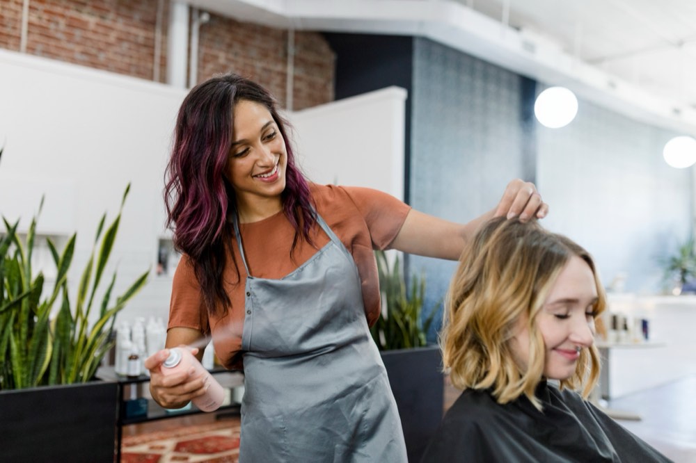 A hairstylist spraying her client's hair in a bright salon